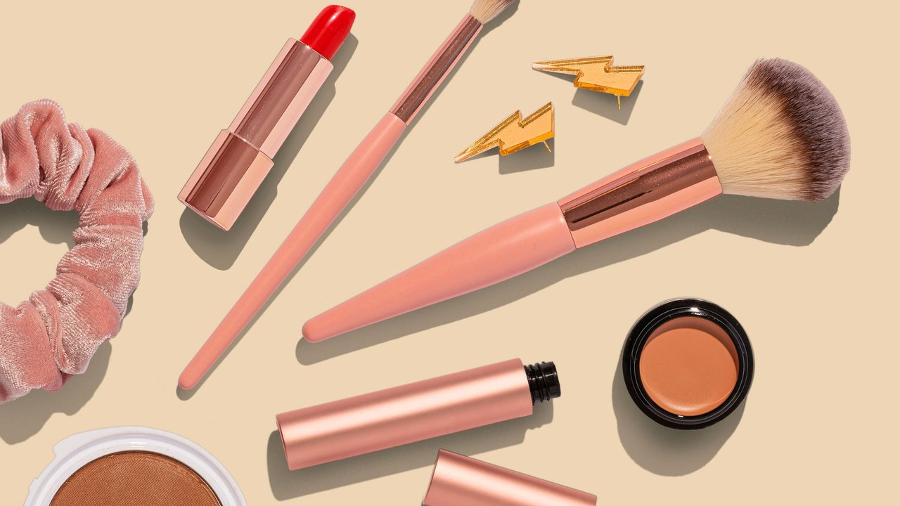 Lipstick, brushes and cosmetics arranged on a pale background