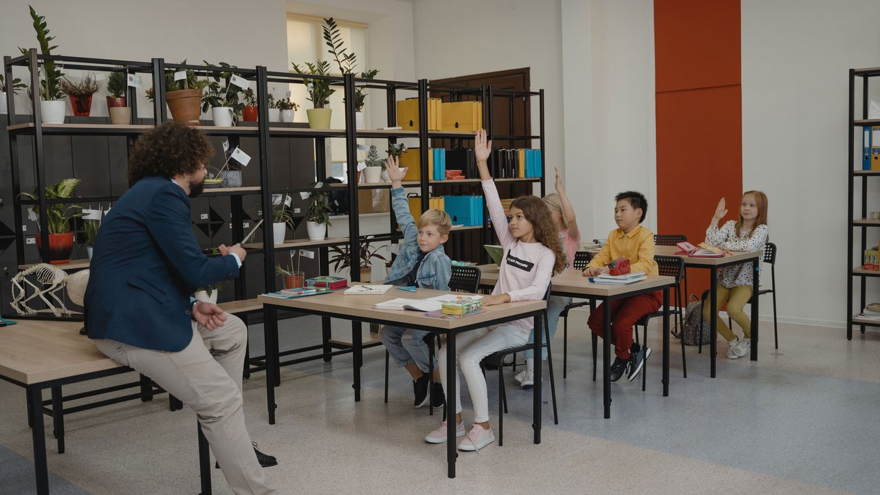 Teacher with young pupils raising their hands in a classroom