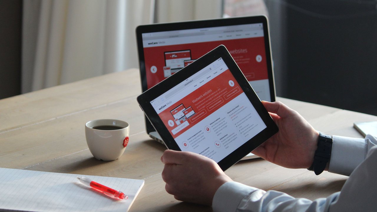 Hands using a tablet and laptop showing a web dashboard