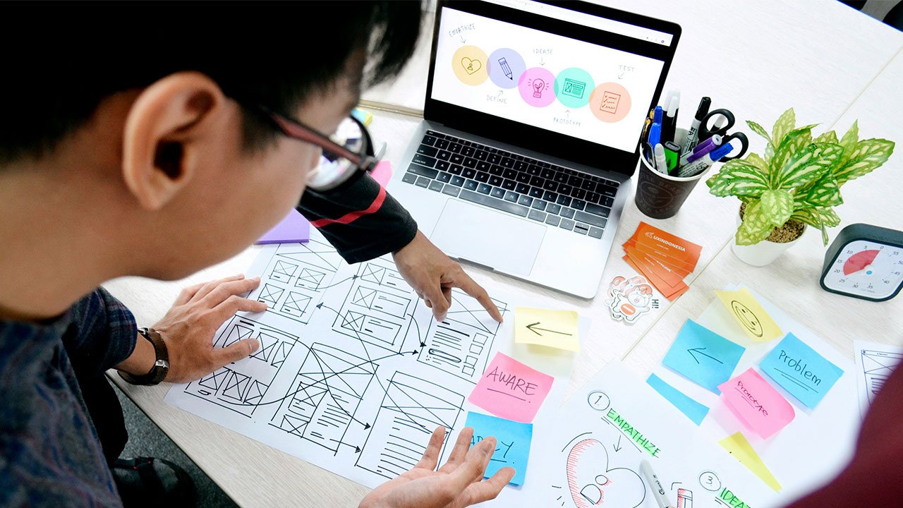 Wireframe sketches and interface components laid out beside a laptop