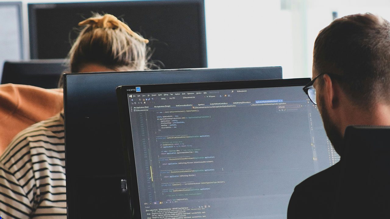 Two developers reviewing code together on a large monitor