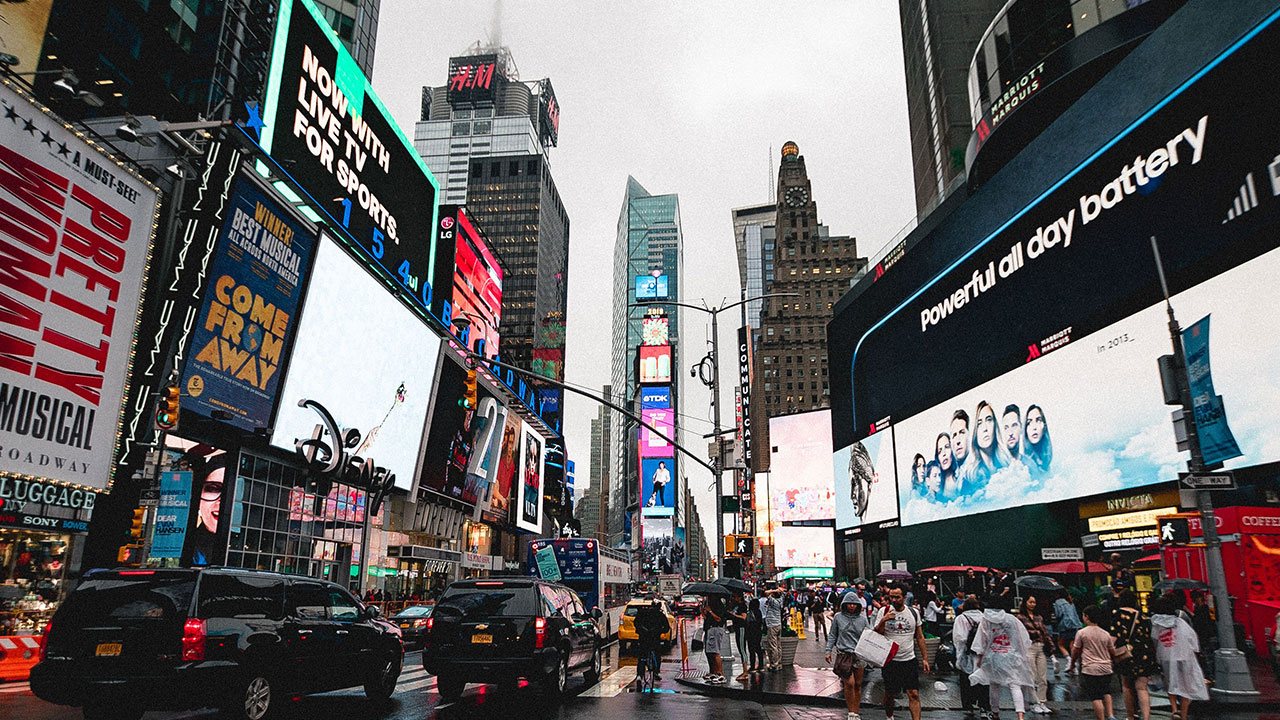 Illuminated advertising billboards above a busy city street